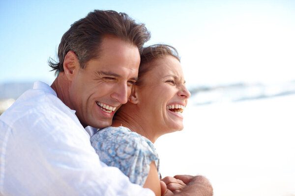 Keep the ones that you love close. A mature man embracing his happy wife from behind as they stand on the beach