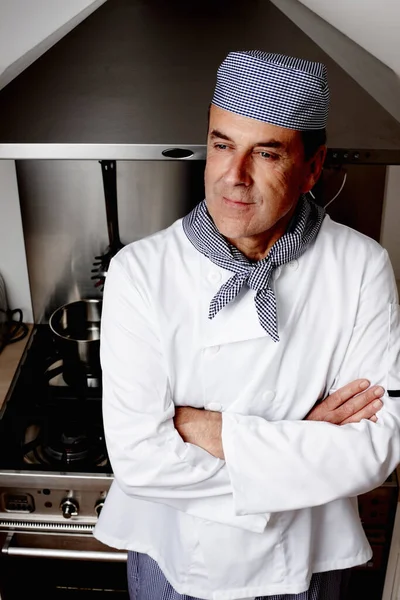 Mature chef with hands folded standing in front of vent hood. Portrait of a happy mature chef with hands folded standing in front of vent hood