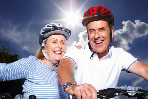 Senior couple with bicycles and protective helmet on a sunny day. Closeup portrait of a cheerful senior couple with bicycles and protective helmet on a sunny day