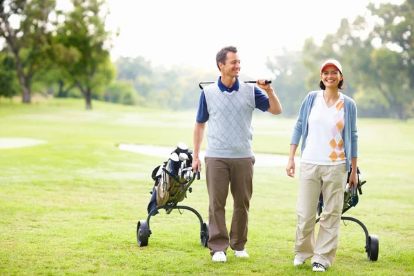 Couple walking on golf course. Full length of couple walking on golf course with golf bags