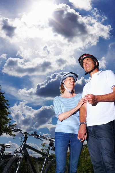 Romantic mature couple standing by bicycle against cloudy sky. Low section of romantic mature couple standing by bicycle against cloudy sky