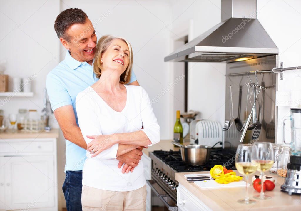 Cheerful mature man embracing wife from behind at kitchen. Portrait of a cheerful mature man embracing wife from behind at kitchen