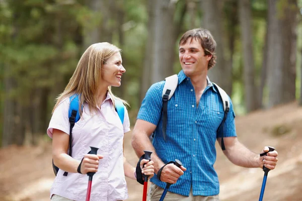 Couple trekking. Smiling couple looking at each other while walking with backpack and trekking poles