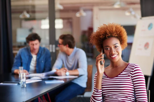 Im in a meeting, can I call you back. A young woman talking on her cellphone during a meeting in an office