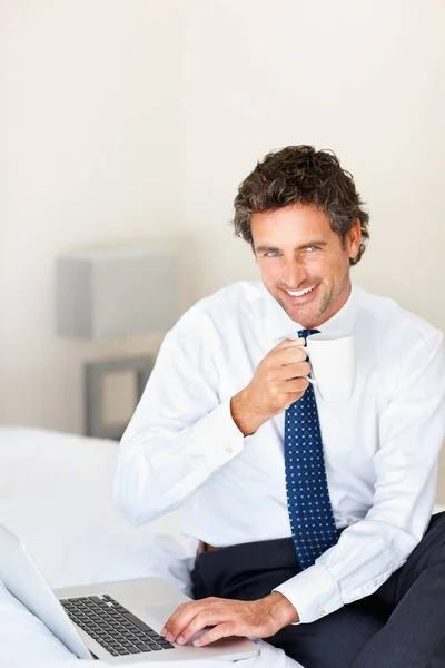 ノートパソコンとコーヒーを片手に微笑む男 笑顔の男はコーヒーを持っているし 自宅でノートパソコンで作業 — ストック写真