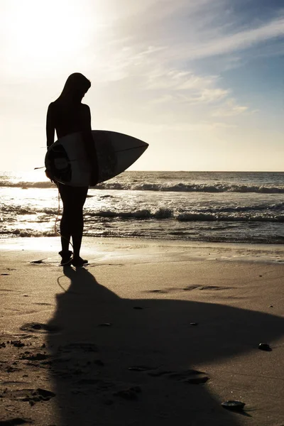 若い女性がビーチでサーフボードを持っています 海岸における若い女性の保持サーフボードの後部ビュー — ストック写真