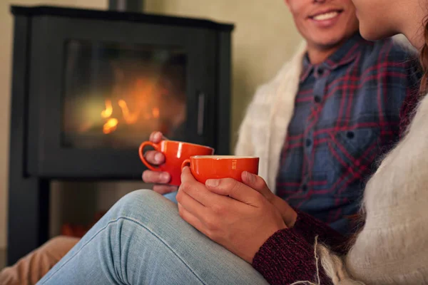 Love warms up the heart. a young couple drinking hot chocolate by the fireplace