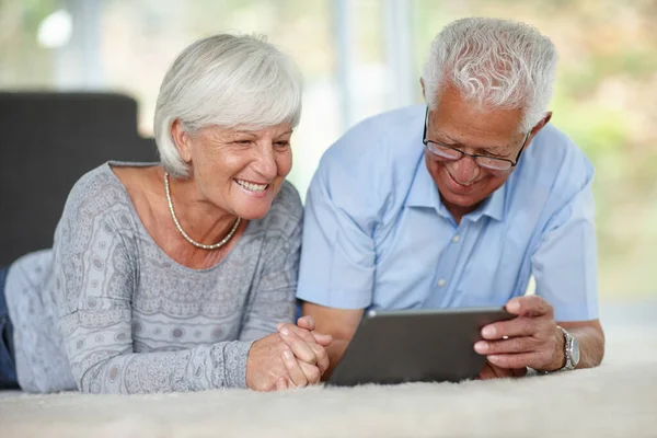 Travel the world with your eye. a senior couple lying on the floor while using a digital tablet