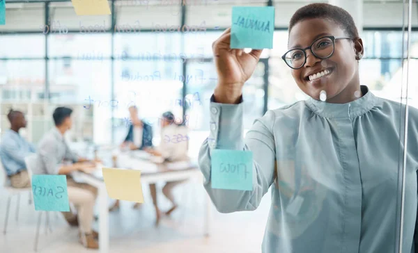 Black woman, post it writing and schedule planning in global business office, marketing startup and creative company. Smile, happy and teamwork leader in meeting with training timeline notes on wall.