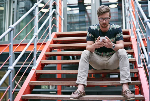 顧客の更新を維持する オフィスの階段に座りながら携帯電話を使っているハンサムな若い男が — ストック写真