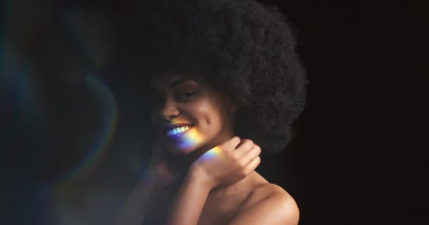自然な髪と笑顔で黒の女性モデルに虹 プリズム光と反射 彼女の顔 歯と体の上にカラフルな照明を持つ幸せな女性は黒の背景にアートライトでポーズ — ストック動画