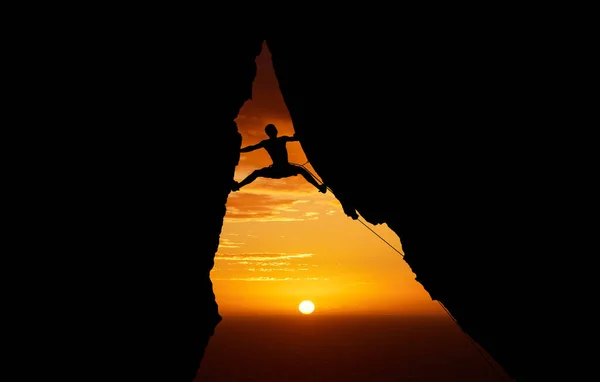 Mountain, sunset and hiking with the silhouette of a man climbing a cliff or rock outdoor in nature. Sun, horizon and sky with a climber outside for exercise, workout and training in the evening.