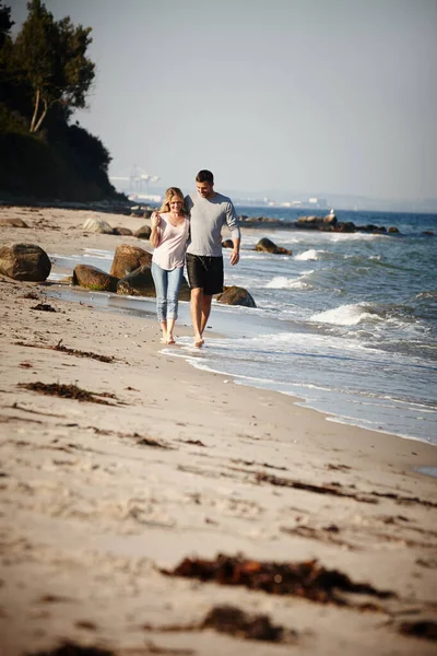 この休暇が一番いい考えだった 砂浜に沿って腕を組んで歩く若いカップルの完全な長さのショット — ストック写真