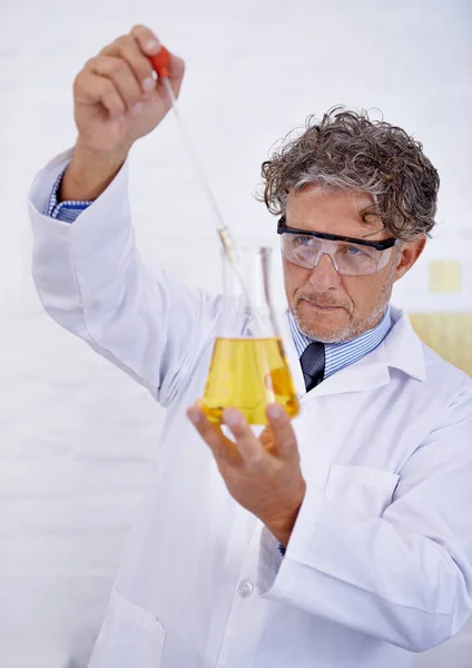 仔细地进行他的实验 一个成熟的科学家把液体倒入实验室的瓶中的剪下来的照片 — 图库照片