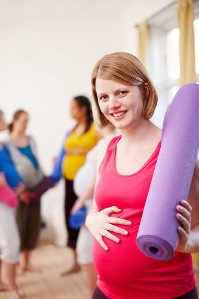 健康な妊娠 背景に女性のグループと運動マットを保持ジムに立つ若い妊婦 — ストック写真