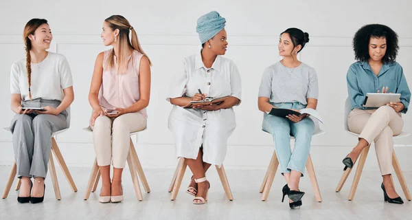 Diversity, interview and business people in waiting room at a job, hiring or recruitment center. Corporate, women and professionals talking with technology in a unemployment office for a work vacancy.