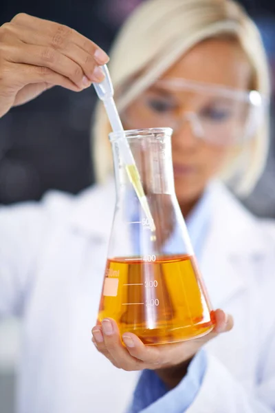 Experimentation is the heart of discovery. a lab technician holding up a beaker of yellow fluid