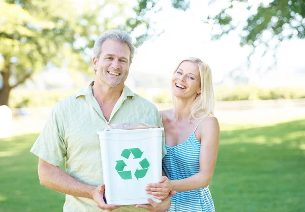 Conservation is our cause. A happy couple standing in a park holding a recycling bin and smiling at the camera