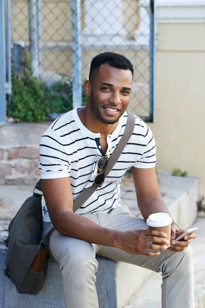 外出先でコーヒーブレイク コーヒーを飲みながら街に座って携帯電話を使うアフリカ系アメリカ人のビジネスマン — ストック写真