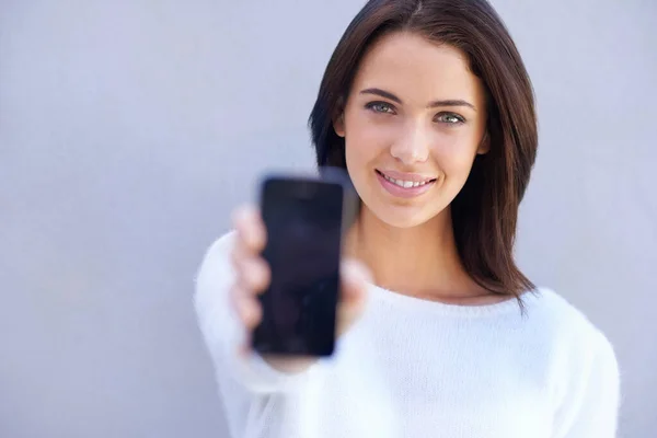 誰もがこの電話を使うべきだ 魅力的な若い女性の肖像画は 灰色の背景に立って 彼女の携帯電話を保持 — ストック写真