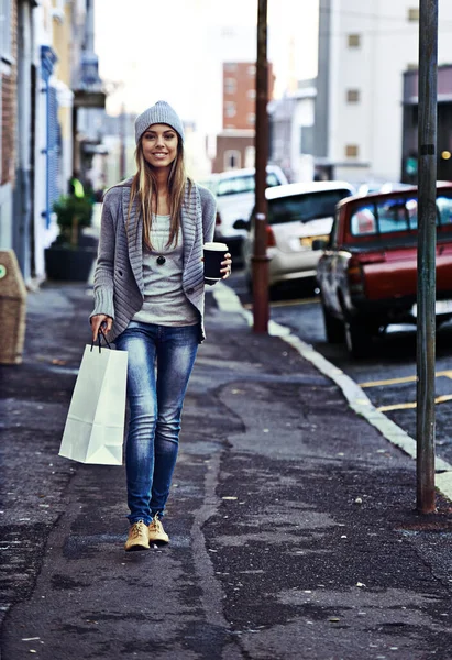 The urban life. Portrait of a beautiful young woman walking with a shopping bag and takeaway coffee in the city