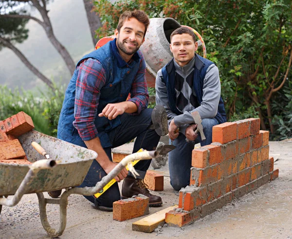 The start of a strong wall - Teaching the basics. Portrait of a bricklayer and his apprentice at work