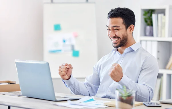 Motivation, success and yes with a business man in celebration and working on a laptop by his desk in the office. Email, good news and smile with a young and happy male employee cheering at work.