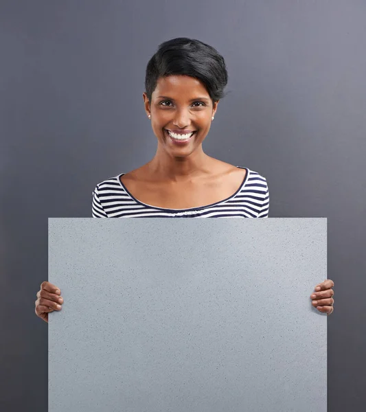 Have I got news for you. Studio shot of a beautiful young woman holding a blank placard against a grey background