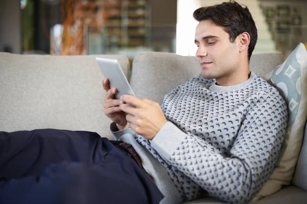 読書が楽になった ソファに座りながらデジタルタブレットを使っている青年が — ストック写真