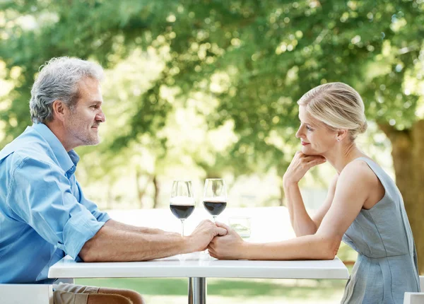 彼らの昼食の日にお金を稼ぐ 幸せな成熟したカップルは 屋外で手を取りながらワインの2つのガラスとテーブルに座って — ストック写真