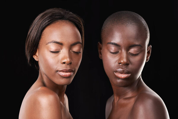 Flawless complexions. Two beautiful african women with their eyes shut standing together against a black background