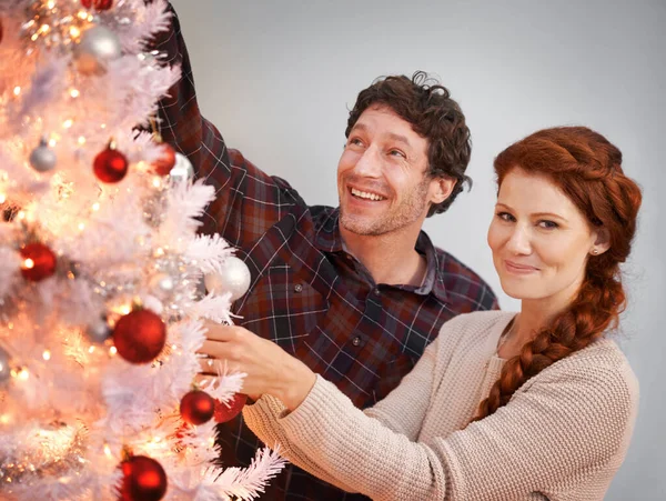 Putting the finishing touches on the tree. Portrait of an affectionate couple decorating a white Christmas tree