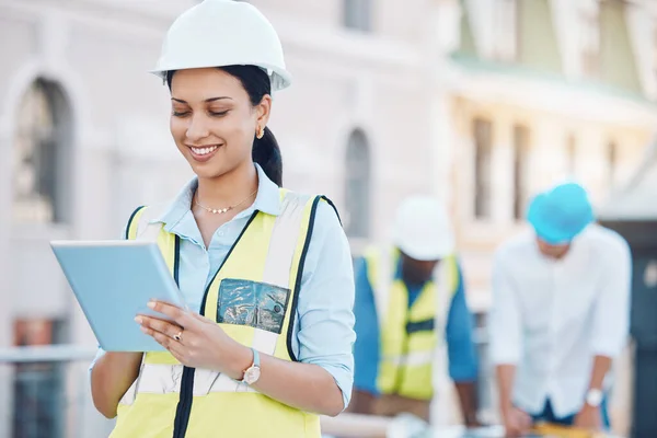 Construction, building and tablet with a woman architect working in the city on a build site with her team in the background. Engineer, designer and architecture with a young female at work online.