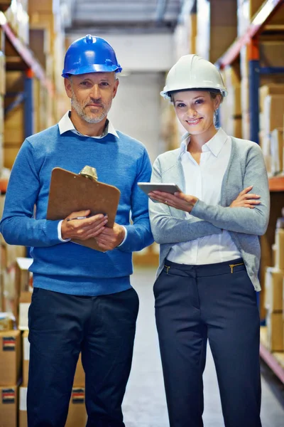 Were a balanced team. Two people wearing hard hats smiling at the camera in a warehouse