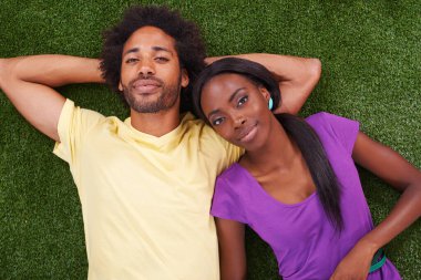 Just unwinding together. A young african couple lying on the grass together clipart
