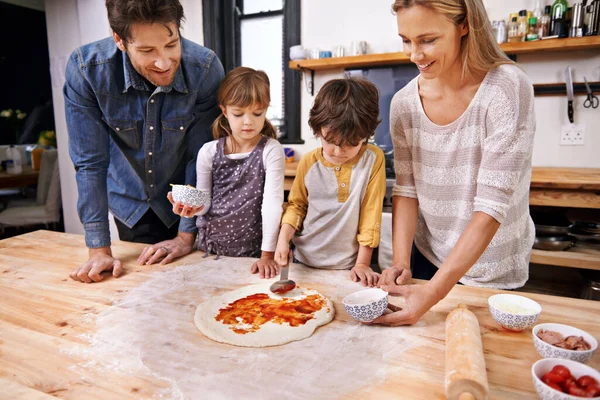 トマトベースを追加する ピザを一緒に家で作る家族 — ストック写真