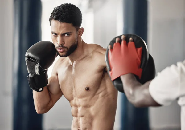 Fitness, training and a man boxing in gym with personal trainer and sparring pads. Health, motivation and exercise, boxer throwing a punch. Fight, muscle and workout with sports gloves in mma studio