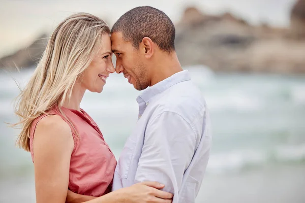 Interracial couple, beach and love bond with forehead together in trust, security or safety. Smile, happy or latino man and woman in hug by ocean or sea water in nature environment for honeymoon date.