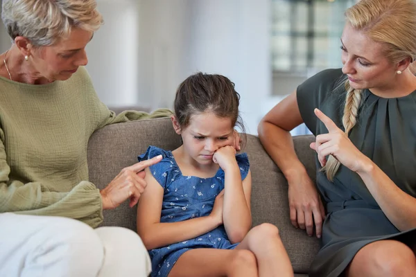 Family, discipline and warning by mother and grandmother hand sign to girl for bad behaviour on a sofa at home. Autism, adhd and communication by parent and daughter in conflict with attitude problem.