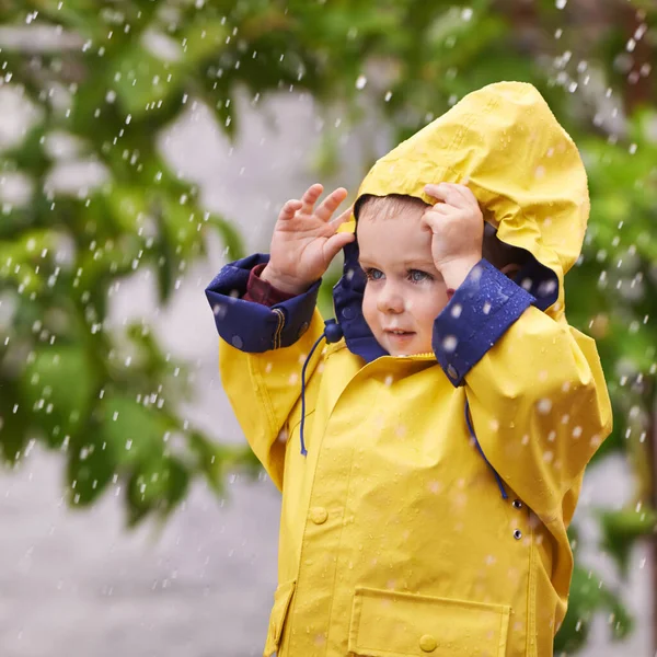 Fascinated by the rain. a young boy playing outside in the rain