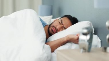 Çalar saati olan yorgun bir adam pazartesi sabahı ruh sağlığı, sağlık ve sağlıklı yaşam için uyanır. Genç uyuyan Asyalı adam yatak odasında erkenden uyanıyor ve esniyor..