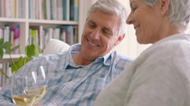 上了年纪的夫妇在他们现代住宅客厅的沙发上喝香槟或葡萄酒 积极向上 开怀大笑的退休老人在家里的沙发上悠闲自在 — 图库视频影像