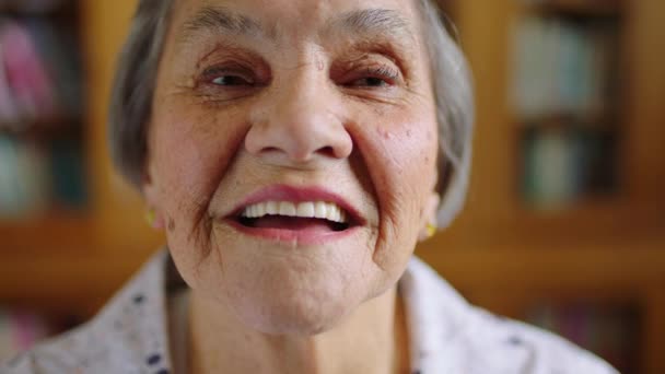 在图书馆里 面对模糊的背景 微笑和智慧的老年女性 一个老年女性的画像 退休时面带微笑 知识渊博 幸福而又积极向上 — 图库视频影像