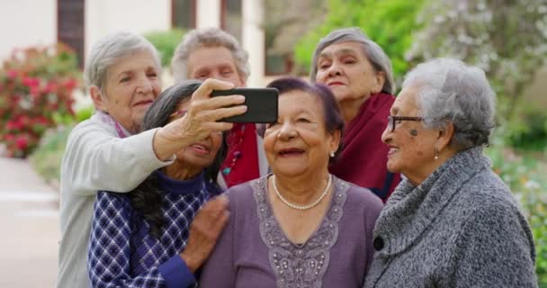一群年事已高的朋友一边站在养老院花园 一边拿着手机自拍 老年家庭公园里 快乐的老年女性在用智能手机在一起的视频通话 — 图库视频影像