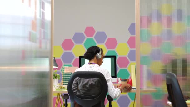 明るいオフィスでコンピュータ上で作業創造的またはグラフィックデザイナーと音楽 デザイン 仕事中にヘッドフォンで聴く女性従業員とのデータ — ストック動画