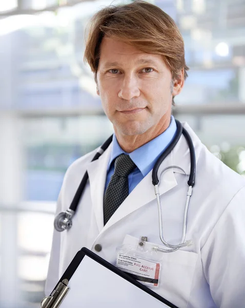 你有适当的健康保险吗 一位英俊的医生站在医院走廊上 手里拿着剪贴板 — 图库照片