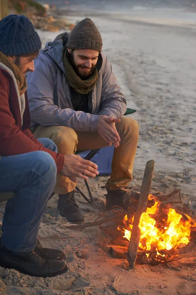 Warming up by the fire. Two young men sitting around a fire on the beach