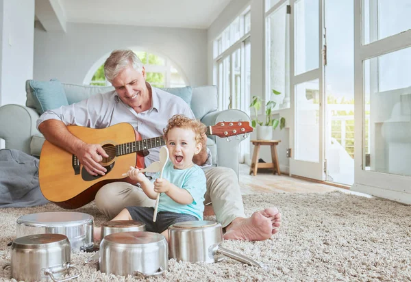 Child drummer with grandfather, guitar and music playing with pot drums in the living room at house. Happy, excited and smile of boy bonding and spending time with his elderly grandpa in family home