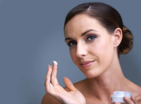 Maintaining her youth through anti-aging skin care products. Portrait of an attractive young woman applying moisturizer to her skin