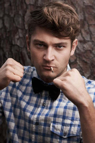 Style with a rough edge. Portrait of a smarty-dressed young man with his arms raised in a fighting pose standing in front of a tree